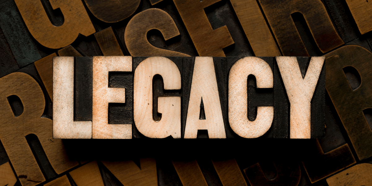 Wooden block letters spelling "LEGACY" on a textured background of assorted letterpress type.