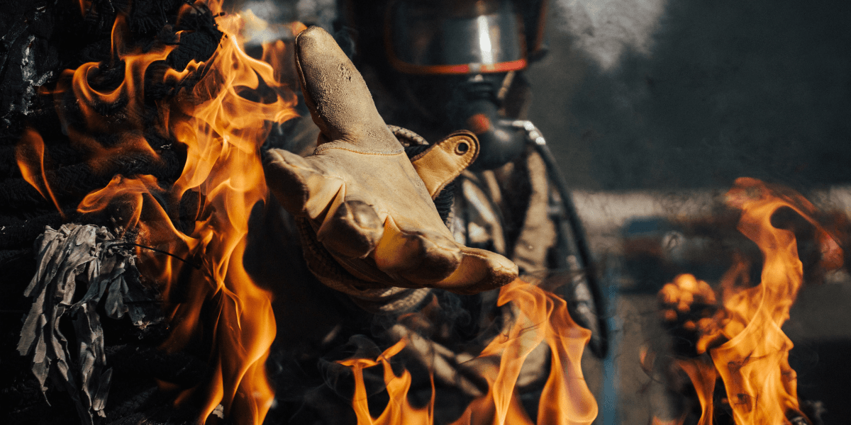 A firefighter reaches out while engulfed in flames, wearing protective gear and gloves