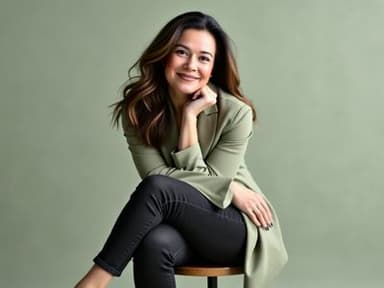 A woman with shoulder-length hair, wearing a green blazer, sitting on a stool, smiling confidently in a calm setting.