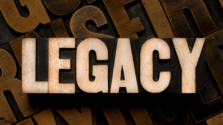Wooden block letters spelling "LEGACY" on a textured background of assorted letterpress type.