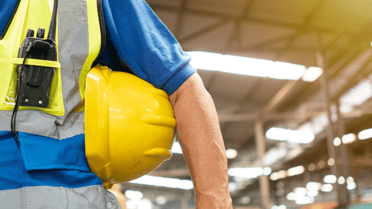 Worker in a blue uniform holding a yellow hard hat in a warehouse setting