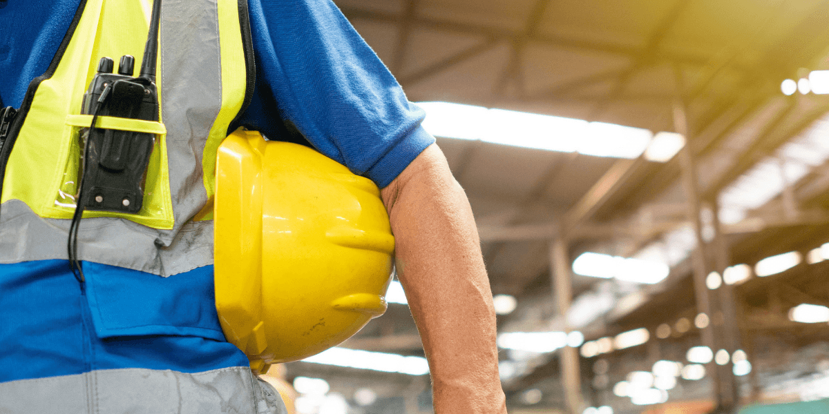 Worker in a blue uniform holding a yellow hard hat in a warehouse setting