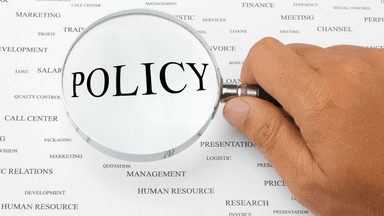 A magnifying glass focusing on the word "POLICY" among various business terms.