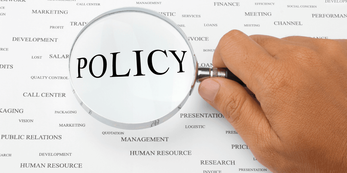 A magnifying glass focusing on the word "POLICY" among various business terms.
