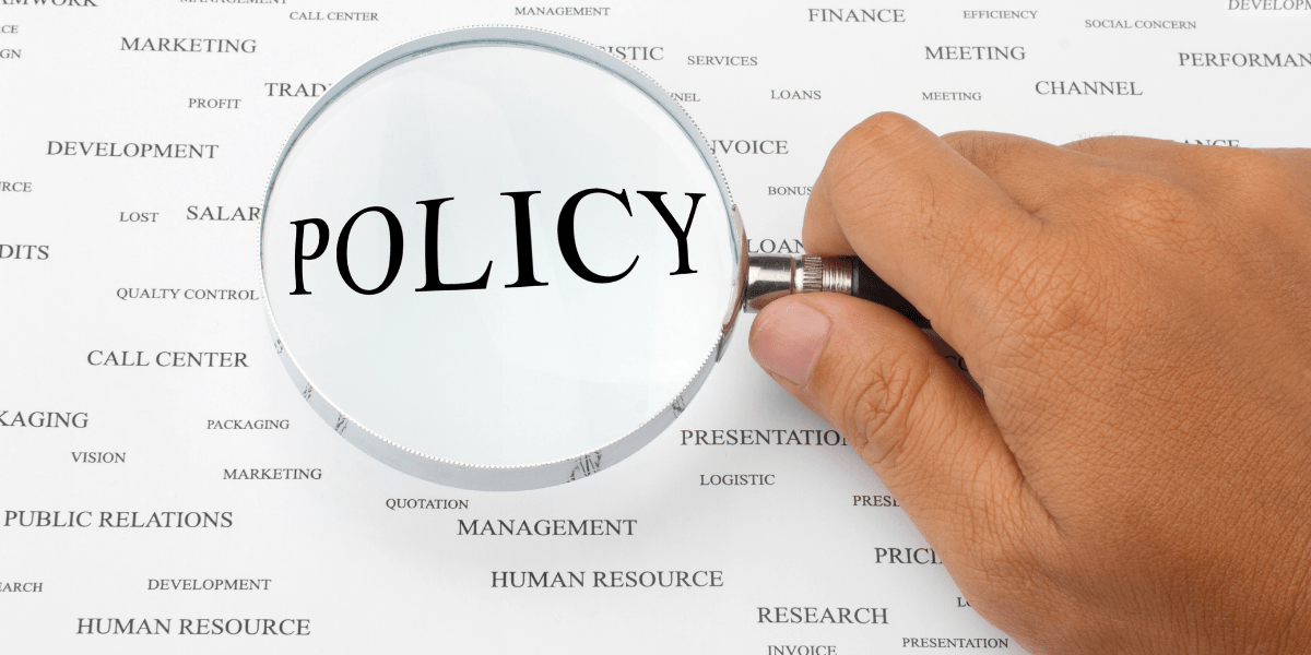 A magnifying glass focusing on the word "POLICY" among various business terms.