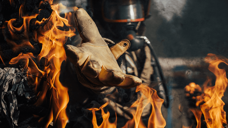 A firefighter reaches out while engulfed in flames, wearing protective gear and gloves