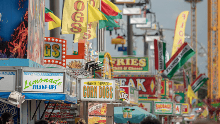 Colorful food stalls at a fair featuring various signs and flags.