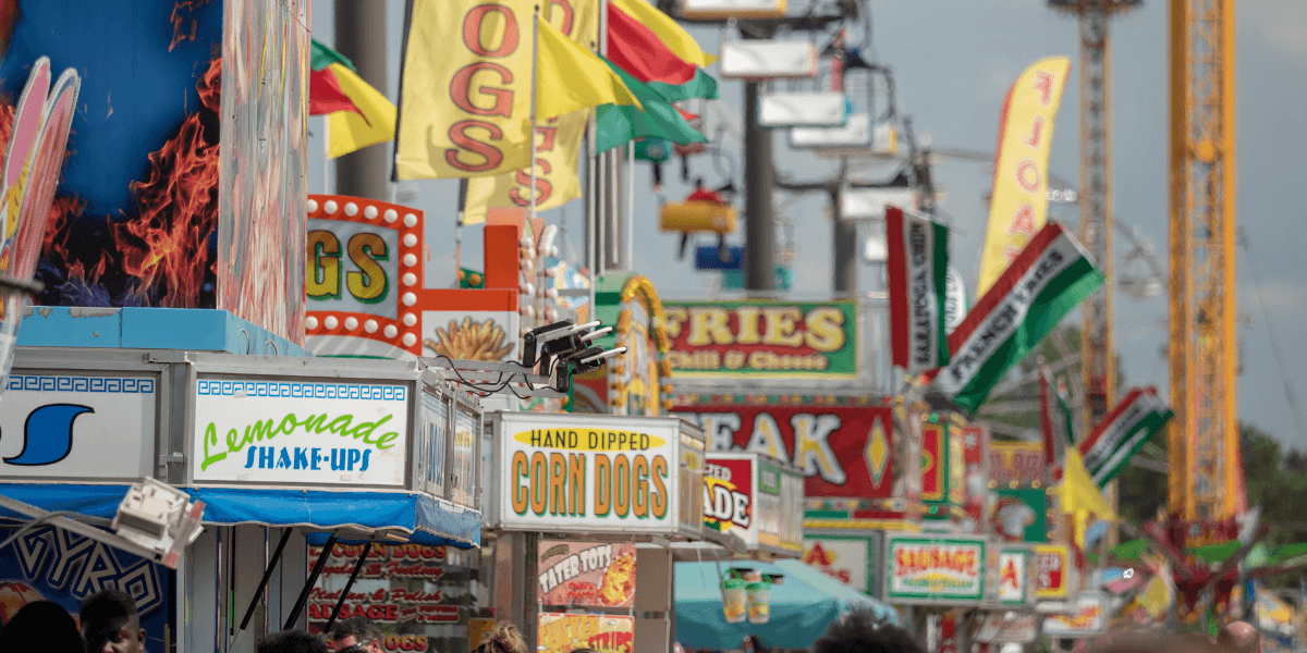 Colorful food stalls at a fair featuring various signs and flags.