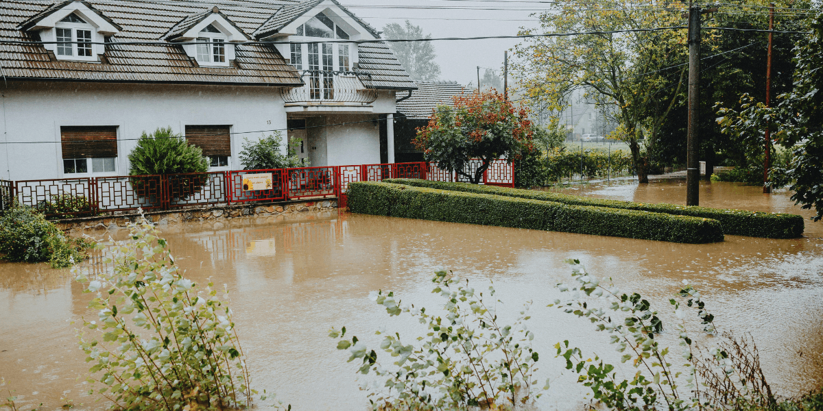 Flooded residential area with water surrounding a house and garden under overcast skies