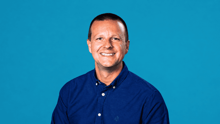 Smiling man in a blue shirt against a solid teal background