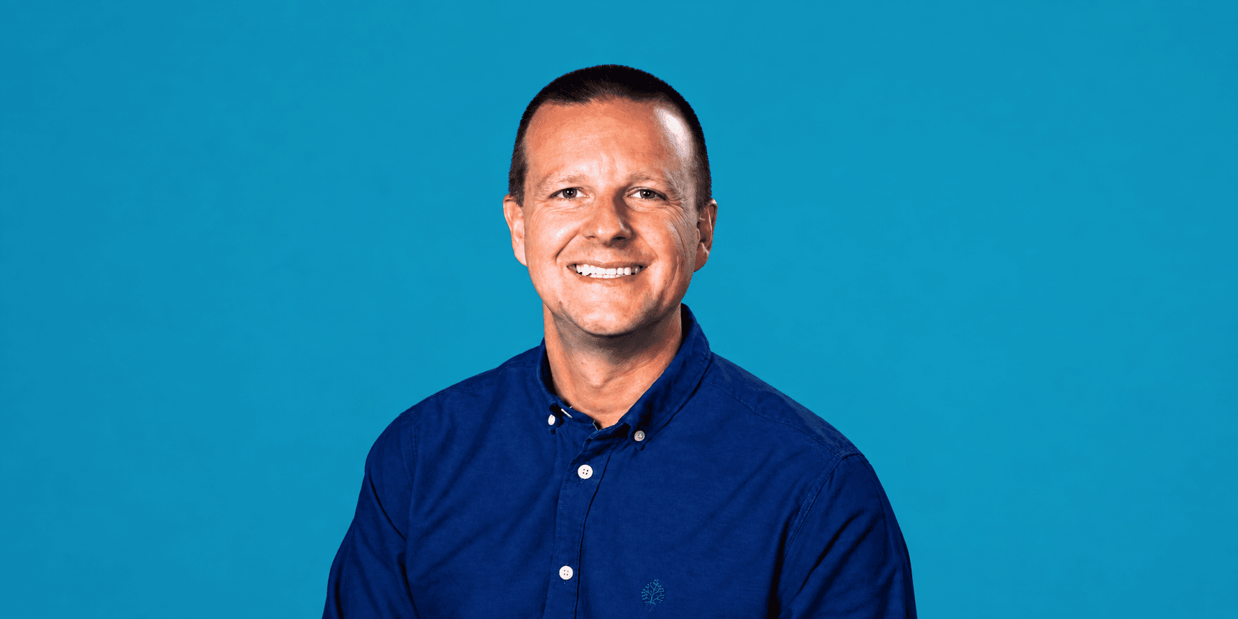 Smiling man in a blue shirt against a solid teal background