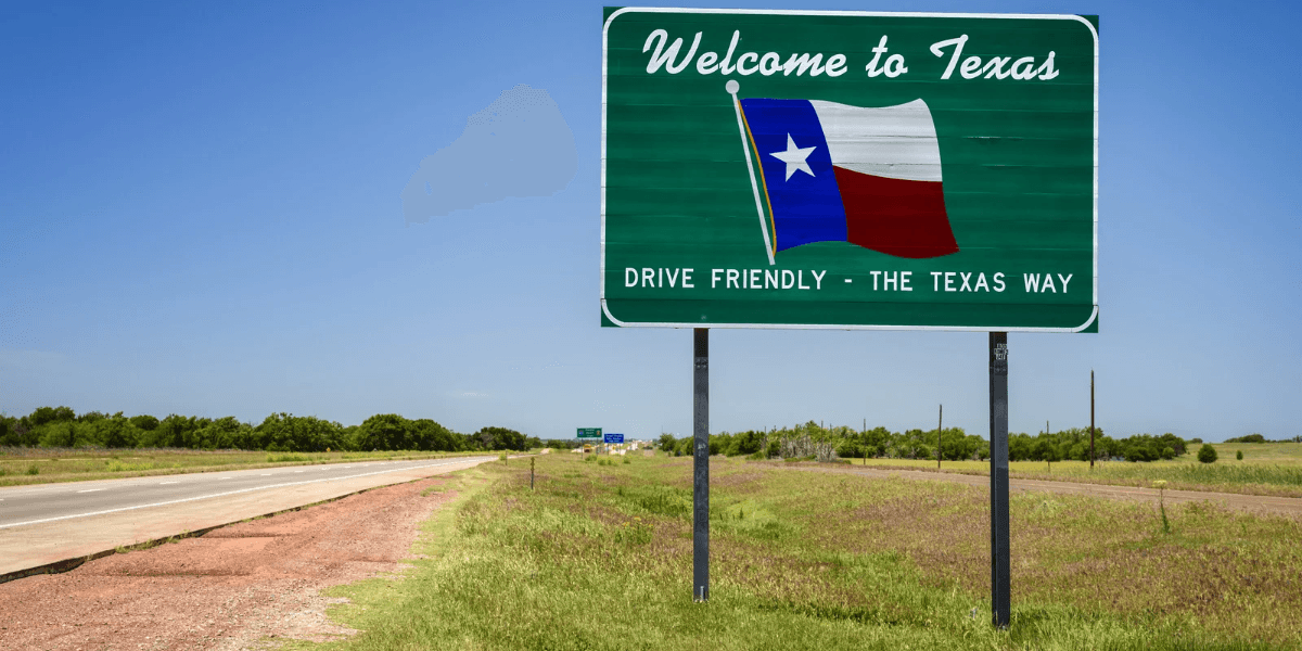 Welcome to Texas sign alongside a highway with green fields in the background