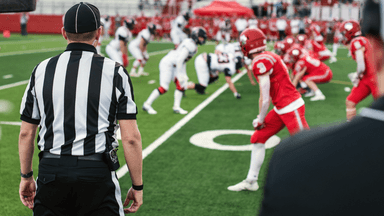 A referee observes two football teams lined up on the field ready for play