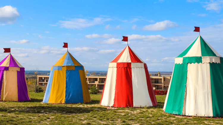 Colorful circus tents with flags set against a blue sky and grassy field