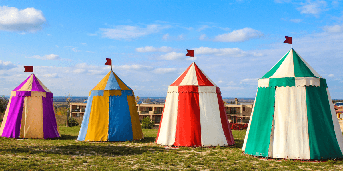 Colorful circus tents with flags set against a blue sky and grassy field