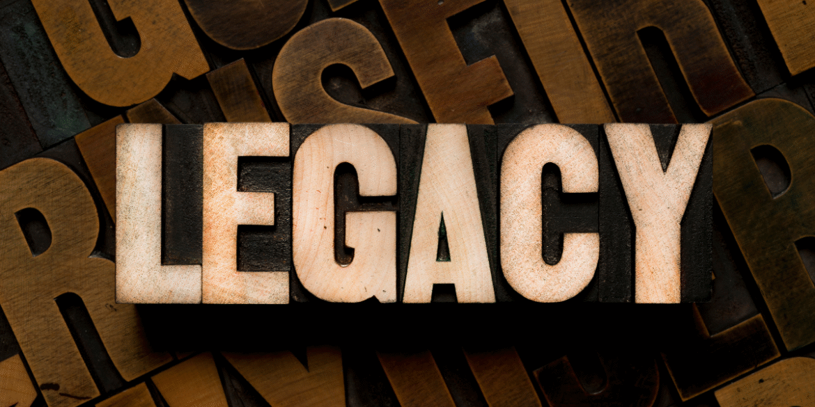 Wooden letterpress blocks spell “LEGACY” against a background of vintage printing type.
